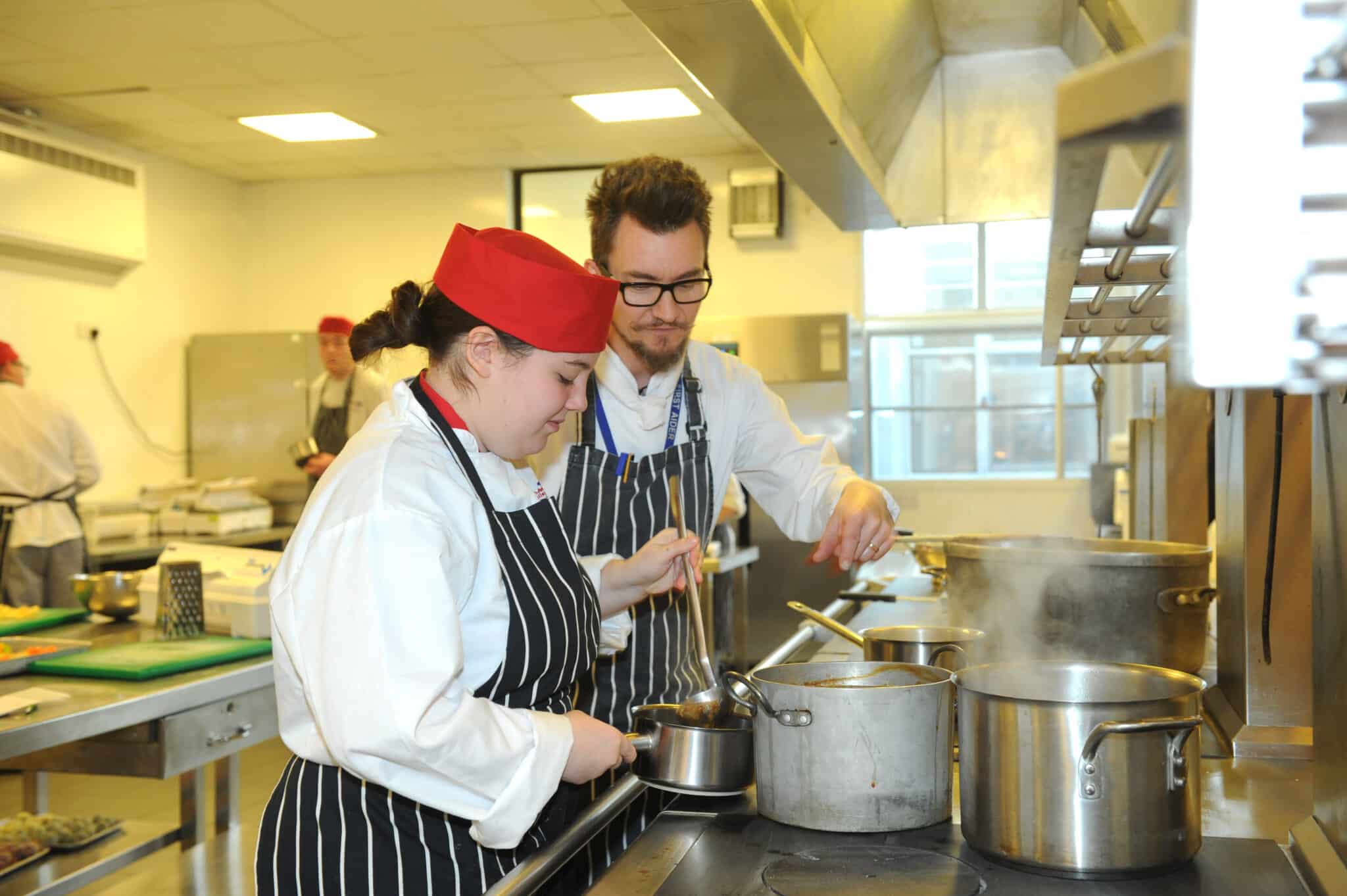 Tutor and student cooking over stove