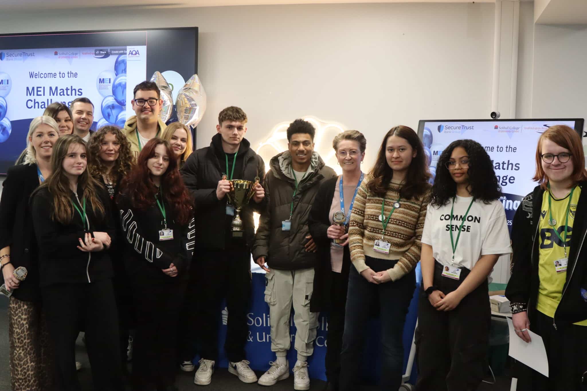 A group of students and their tutors smiling at the camera holding a trophy.