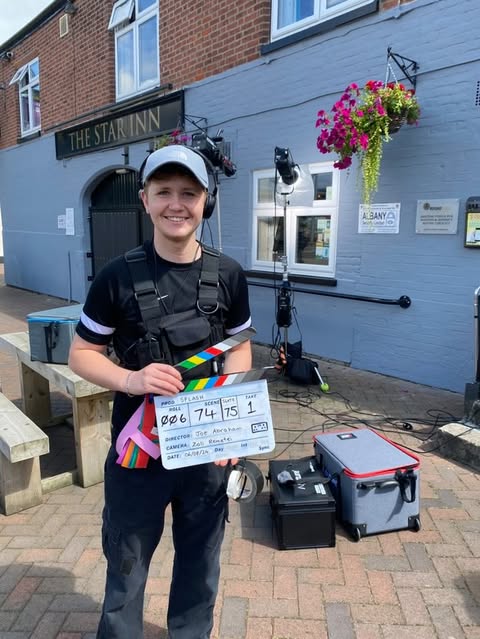 Man smiling on step holding a film clapper board