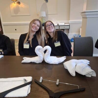 2 students smiling behind 2 towel swans