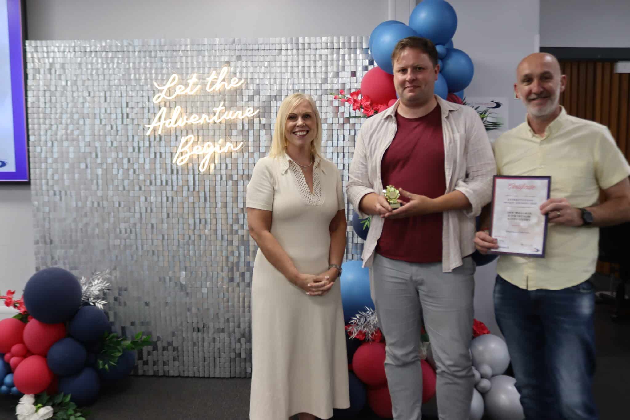 three people standing in front of sparkly backdrop and balloons